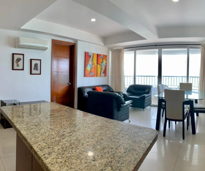 Vista desde la cocina hacia la sala con proyeccion al balcón del apartamento vacacional 1003 Andrea para un verdadero descanso frente al caribe